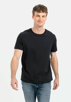 Schwarzes Baumwoll-T-Shirt mit Rundhalsausschnitt, kurzen Ärmeln und einem dezenten Logo. Kombiniert mit blauen Denim-Jeans. Weicher Stoff, taillierte Passform.