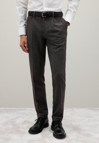 Pantaloni grigi su misura con un sottile motivo a quadri, fronte plissettato e una texture liscia. Abbinato a scarpe di pelle nere e una cintura nera.