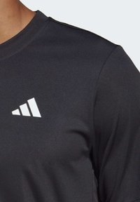 Camiseta deportiva negra con cuello redondo, mangas cortas y un logo triangular blanco en el pecho. Tela suave y ligera.