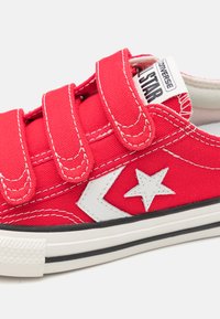 Deportiva de lona roja con tres cintas de velcro, logo de estrella blanca, costura en contraste, capucha de goma y suela de goma negra.