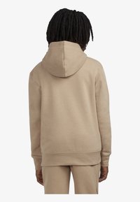 Sudadera con capucha beige de textura suave, con bolsillo tipo canguro y puños de canalé. La parte trasera muestra un diseño simple sin marcas visibles.