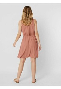 Helles pinkes ärmelloses Kleid mit elastischem Taillenbund, fließendem Rock, aus einem glatten Stoff gefertigt und mit flachen Sandalen getragen.