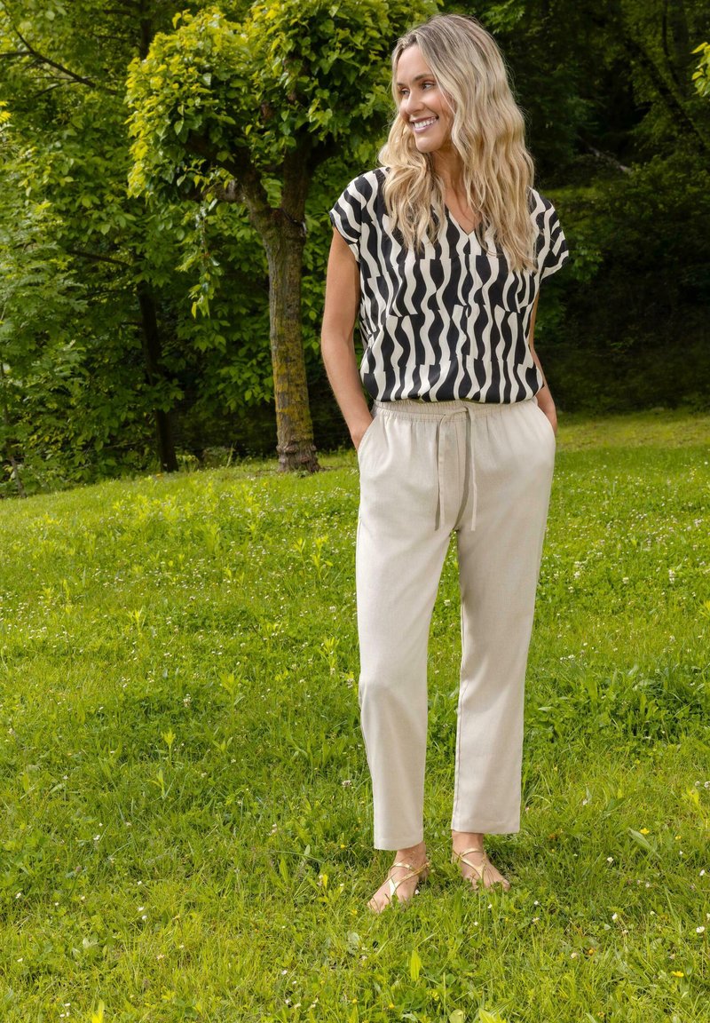 Top a maniche corte con motivo in bianco e nero abbinato a pantaloni beigi elasticizzati in vita e sandali marroni con cinturini, sullo sfondo di un prato.