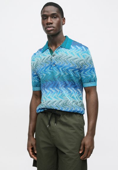 Pánské polo tričko s krátkým rukávem v modro-zeleném vlnkovém vzoru, s knoflíkovou légou a žebrovaným límcem. Kombinováno s tmavě zelenými šortkami.