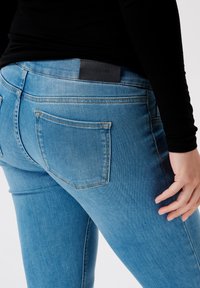 Blå denimjeans med en lätt blekning, med rak passform, femficksdesign och en svart läderlogg på midjebandet.