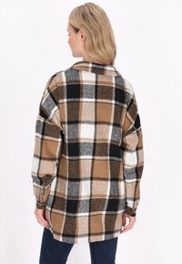 Brun och svart rutig flanellskjorta med vita detaljer, avslappnad passform, sänkta axlar och långa ärmar. Knappdetaljer vid handleden.