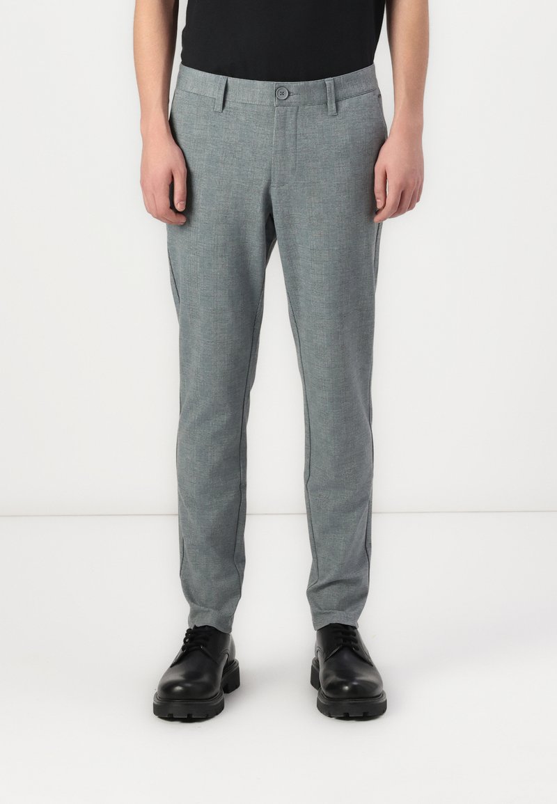 Gray patterned trousers feature a slim fit, flat front, and button closure, with side pockets and rolled cuffs, paired with black shoes.