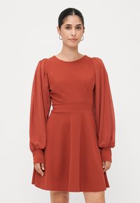 Kopparfärgad klänning med en figurnära bodice och voluminösa, puffärmar. Tillverkad av ett slätt tyg, flikskirt som faller ovanför knäet.
