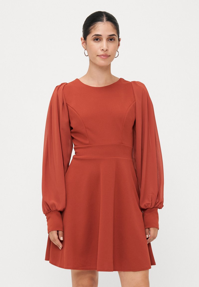 Kopparfärgad klänning med en figurnära bodice och voluminösa, puffärmar. Tillverkad av ett slätt tyg, flikskirt som faller ovanför knäet.