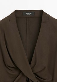 Detail tmavě hnědé halenky Massimo Dutti s výstřihem do V a nařaseným, překrouceným předním detailem. Značkový štítek viditelný u límečku.