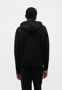 Czarna bluza z kapturem o luźnym kroju, wyposażona w kaptur z regulowanym sznurkiem, ściągacze na mankietach i u dołu. Miękka w dotyku, gładka, idealna do codziennego noszenia.