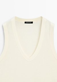 Crème-kleurig mouwloos topje van zachte stof, met een diepe V-hals en een subtiele textuur. Gemarkeerd met een zwart label met de tekst "Massimo Dutti."