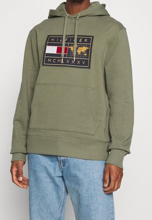 Sudadera color verde oliva hecha de suave algodón, con un bolsillo tipo canguro en la parte frontal y un parche de logotipo gráfico con colores rojo, blanco y detalles dorados.