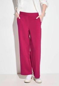 Fuchsia wijde broek met een elastische tailleband, voorzien van zijzakken. Gecombineerd met witte sneakers voor een casual look.