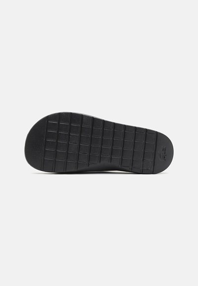 Semelle de chaussure en caoutchouc noir avec un motif de texture et des rainures carrées et rectangulaires pour l'adhérence. Pas de marque visible.