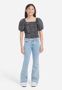 Crni top s napuhanim rukavima s bijelim točkicama, u kombinaciji sa svijetloplavim širokim trapericama i bijelim tenisicama. Jednostavan dizajn i opušteni kroj.