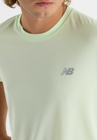 Vaaleanvihreä urheilupaita, jossa on pyöreä kaulus, teksturoitu kangas ja pieni harmaa logo rinnassa. Rentoa tyyliä, jossa on lyhyet hihat.