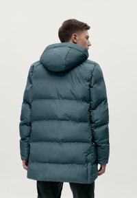 Giacca a vento in teal, con cappuccio e design trapuntato orizzontale. Finitura opaca con tasche laterali e polsini regolabili.