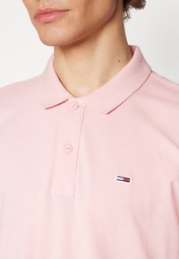 Polo shirt rosa chiaro con tessuto texture. Presenta una pattina con tre bottoni e un piccolo logo ricamato sul lato sinistro del petto.