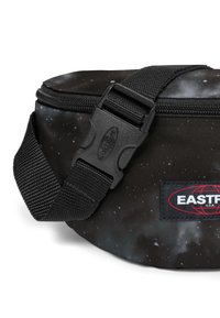 Černá ledvinka vyrobená z odolného materiálu s potiskem galaxie, vybavená texturovaným popruhem a plastovou přezkou. Viditelné logo Eastpak.