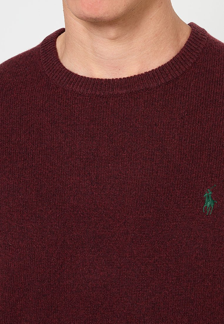 Pull en tricot bordeaux avec un col rond, doté d'un logo brodé vert sur la poitrine et d'un tissu texturé.