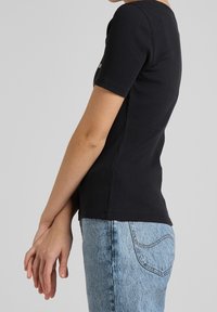 Sort ribbet kortærmet top med en tætsiddende design, parret med lyseblå jeans med en klassisk lomme-syning detalje.
