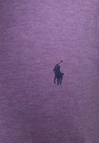 Fialová texturovaná látka s jemným melírovaným vzorem. Na spodní levé straně je malý tmavě modrý vyšívaný motiv hráče polo.