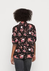 Blusa preta com padrão floral, mangas curtas e volumosas, apresentando flores rosas e brancas, colarinho e uma bainha ligeiramente curva.