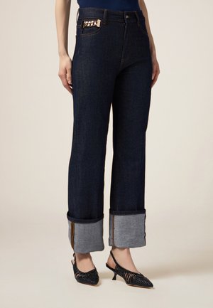 Donkerdenim wijde jeans met omgeslagen zoom in lichtblauwe stof. Beschikt over een gouden kettingdetail op de voorzak.