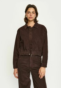 Jachetă din catifea maro cu guler, închidere cu fermoar și tiv elastic. Are dungi verticale texturate și mâneci lungi. Potrivită pentru îmbrăcăminte casual.