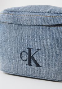 Borsa in denim con forma rettangolare strutturata, colore blu chiaro, cuciture visibili e logo ricamato 'cK' in blu scuro.