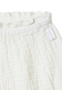 Pantalons en mousseline blanche présentant un tissu doux et texturé, une taille élastique et une petite étiquette cousue avec le logo "noppies".