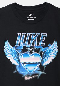 Μαύρο χαλαρό μπλουζάκι Nike με μπλε και λευκό γραφικό σχέδιο φτερών και καρδιάς. Το κείμενο αναγράφει "NIKE" και "ΘΕΑ ΤΗΣ ΝΙΚΗΣ".