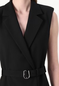 Black sleeveless dress with a sharp collar and double-breasted design. Features a belted waist with a silver metal buckle accent.