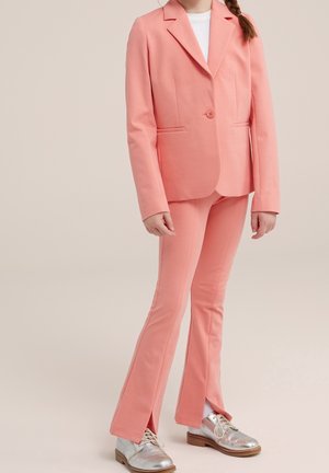 Meisje draagt een koraalroze pak met een blazer met één knoop, bijpassende uitlopende broek met voorsplitten, witte sokken en metallic zilveren schoenen.