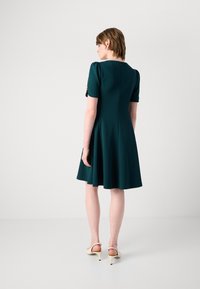 Dark green fitted dress with short puff sleeves, a cinched waist, and a flared skirt. Features a discreet back zipper closure.