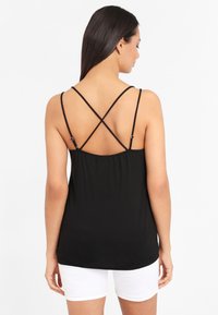 Black sleeveless top with crisscross straps at the back, made of soft fabric, featuring a loose fit and gathered detail at the waist.