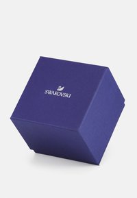 Lilla tekstureret gaveæske med pyramideform, der har et sølv Swarovski-logo på forsiden. Slankt og kompakt design.