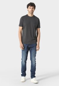 Sötét szürke, rövid ujjú póló, amelyen egy kis logó található a mellrészen, világoskék farmernadrággal és fehér sportcipőkkel párosítva. Egyszerű dizájn és illeszkedés.