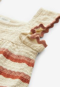 Cremefarvet strikket babydress med rust- og lyserøde vandrette striber og flæser på ærmerne kantet med rustbrunt garn.