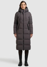 Pitkä, tikattu toppatakki tummanharmaana, jossa on huppu, edessä vetoketjusuljenta ja kaksi vetoketjullista sivutaskua, yhdistetty mustiin saappaisiin.