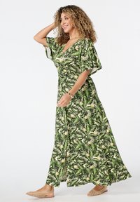 Maxi-jurk in groen met een tropische bladeren- en ananasprint. Korte mouwen, V-hals, vloeiende vorm, zachte stof en een uitsnijding aan de zijkant.