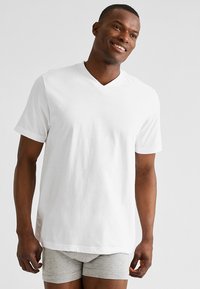 T-shirt blanc à manches courtes en coton léger, avec un col en V, présentant une coupe décontractée et une texture lisse, associé à un boxer gris.