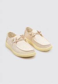 Zapatos de tela beige con perfil bajo, punta redonda y suela de goma amarilla. Detalle de atado en la parte delantera y un interior con estampado floral.