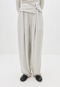 Hellegraue, locker sitzende, gefaltete Sweatpants mit weicher Textur, kombiniert mit schwarzen Slippern. Schlichtes Design und lässiges Erscheinungsbild.