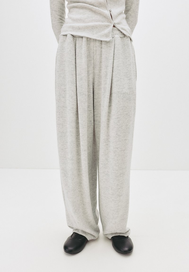 Hellegraue, locker sitzende, gefaltete Sweatpants mit weicher Textur, kombiniert mit schwarzen Slippern. Schlichtes Design und lässiges Erscheinungsbild.
