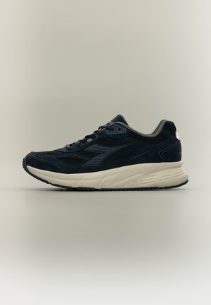 Chaussure de course noire et gris foncé avec tige en mesh et en daim, semelle blanche amortie, et fermeture à lacets sur un fond neutre.