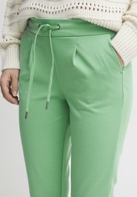 Grüne Sweatpants mit einem Zugbandbund, zwei Seitentaschen, glattem Material und Falten für zusätzlichen Detail.