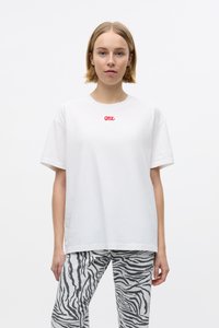Witte katoenen T-shirt met korte mouwen, met een kleine rode grafische tekst "ONE" op de borst. Gecombineerd met grijze broek met zebraprint.