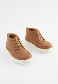 Et par brune høj-top sneakers med tan snørebånd og hvide gummisåler på en helt hvid baggrund.